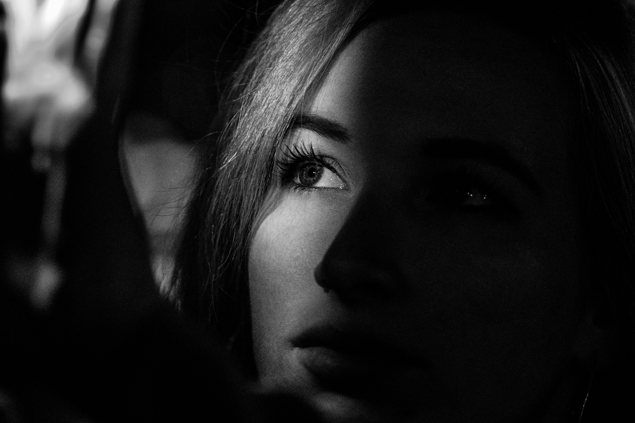 Black-and-white close-up of a woman's face looking at a light source. Only the right eye is lit up, the rest fades into the shadows.
